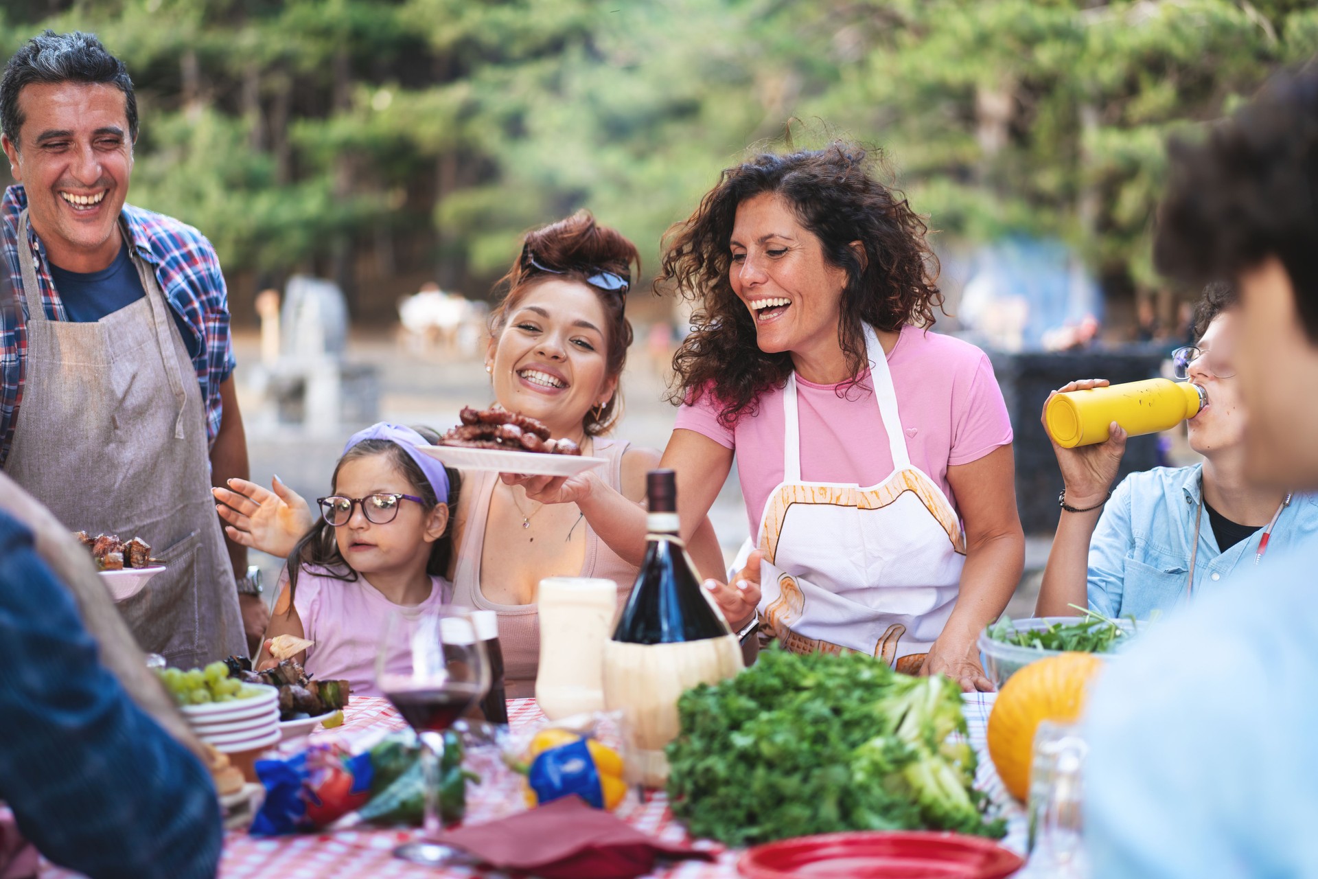 Joyful family barbecue, multigenerational outdoor dinner, diverse group laughing at summer picnic